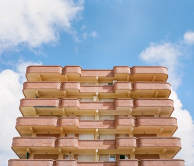 Stacked brick balconies of a coastal apartment block rising into a deep blue sky