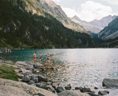 Two friends wading from the rocky shore of a glassy alpine lake in the Pyrenees