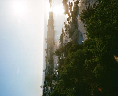 Sun flaring over Clifton's granite-rimmed coves at the end of the day