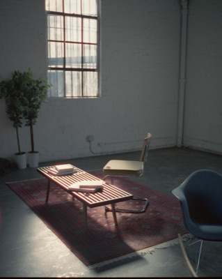 Mid-century slatted bench and chair arranged on a Persian rug in a sunlit studio