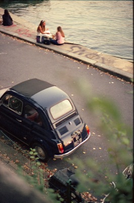 Classic Fiat 500 parked along the Seine while friends picnic at the river's edge