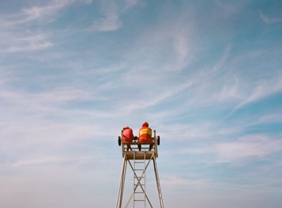 Two lifeguards keeping watch from a high tower against a sweep of cirrus cloud