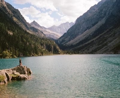 Lone figure standing on a rock outcrop above a turquoise alpine lake in the Pyrenees